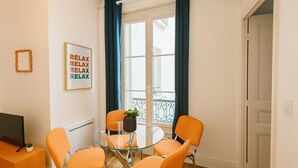 Ein Zimmer mit einem Glastisch, um den vier orangefarbene Stühle stehen, einer kleinen Topfpflanze und einem gerahmten Schild mit der Aufschrift 'RELAX' an der Wand.