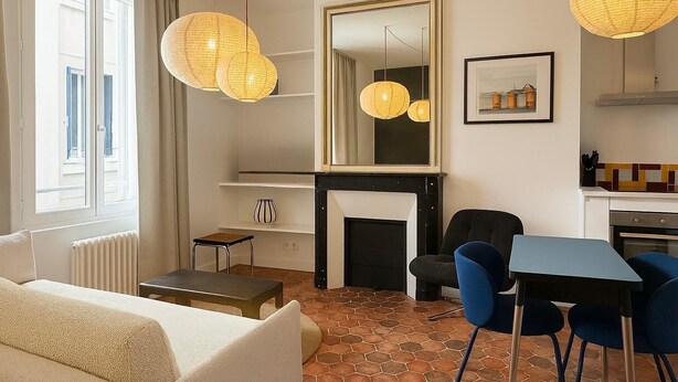 A modern living room with a fireplace, a dining area with blue chairs, and a kitchen area. - Appartement rue Montorgueil au Halles - Paris 1 (Paris)