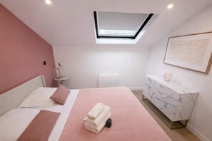 A bedroom with a skylight, a bed with pink bedding, a marble bedside table, and a wall-mounted artwork. - Sejour familial spacieux a Aubervilliers pour 4 (Aubervilliers)