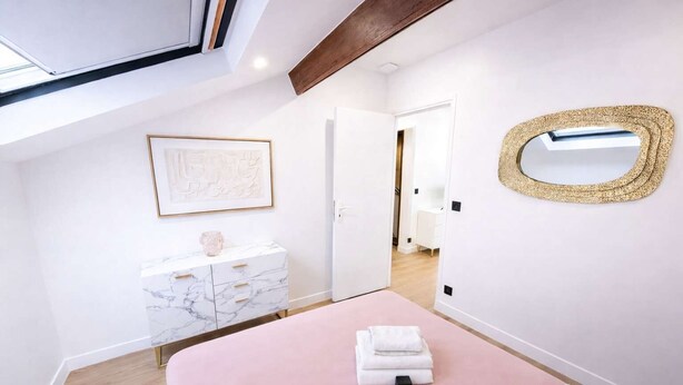 Un dormitorio con una cama, un tocador de mármol, una obra de arte enmarcada, un espejo y una puerta que da a otra habitación.