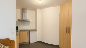 Una cocina compacta con lavavajillas integrado, estufa y microondas. Hay un armario de madera con dos puertas y una pequeña encimera.