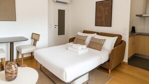 Un dormitorio moderno con cama, mesita de noche, silla y una pequeña mesa redonda con un florero.