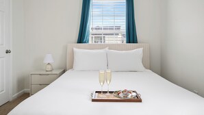 A hotel room with a bed, two champagne glasses, a tray with pastries, and a nightstand with a lamp. - Holy City Hideaway | Minutes from Everything (North Charleston)