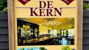 Een bordje voor Grand-Café De Kern met foto's van het interieur en exterieur, en een welkomstboodschap in het Nederlands.