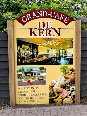 A sign for Grand-Café De Kern with interior and exterior photos, and a welcome message in Dutch. - Rustic Woodland Cabin Sven (Putten)