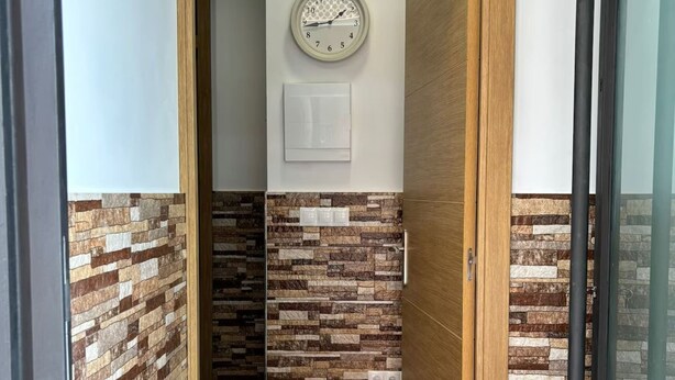 A hallway with a wooden door, a wall clock, and a textured wall.