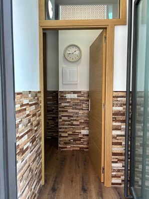 A hallway with a wooden door, a wall clock, and a textured wall.