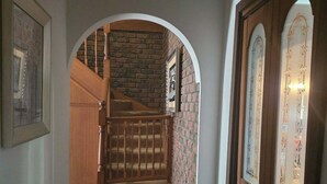 A hallway with a wooden staircase leading to a brick wall.