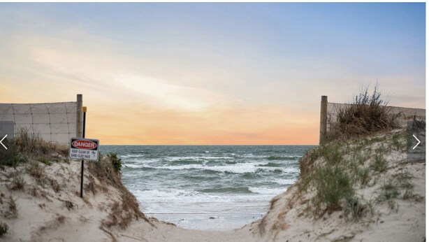 A beach with a warning sign and a fence.