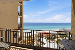 A balcony with a view of the ocean and beach, a pool, and a building with a red roof. - 10th Floor Westwinds Updated 2BR/2BA Condo at Sandestin (Miramar Beach)