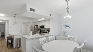 Una cocina moderna con armarios blancos, una isla central y un comedor con una mesa redonda y sillas blancas.
