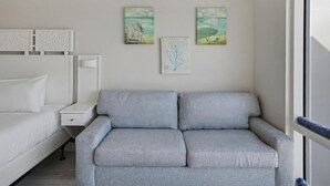 A bedroom with a grey sofa, a white bed, and two wall art pieces. - Studio condo on 7th Floor at Luau in Sandestin Golf & Beach Resort (Miramar Beach)