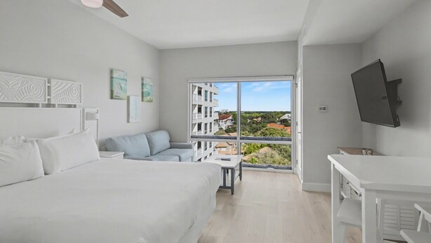 A modern hotel room with a large bed, a sofa, a desk, and a balcony with a city view. - Studio condo on 7th Floor at Luau in Sandestin Golf & Beach Resort (Miramar Beach)