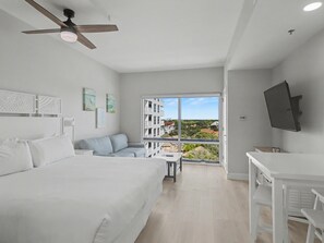 Una habitación de hotel moderna con una cama grande, un sofá, un escritorio y un balcón con vistas a la ciudad.