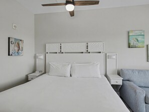 Un dormitorio ordenado con cama, mesitas de noche, ventilador de techo y obras de arte en las paredes.