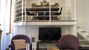Uma sala de estar estilo loft com teto alto, área de jantar com corrimão branco e TV fixada na parede.