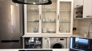 Uma cozinha moderna com geladeira de aço inoxidável, lava-louças, máquina de lavar e um laptop no balcão.