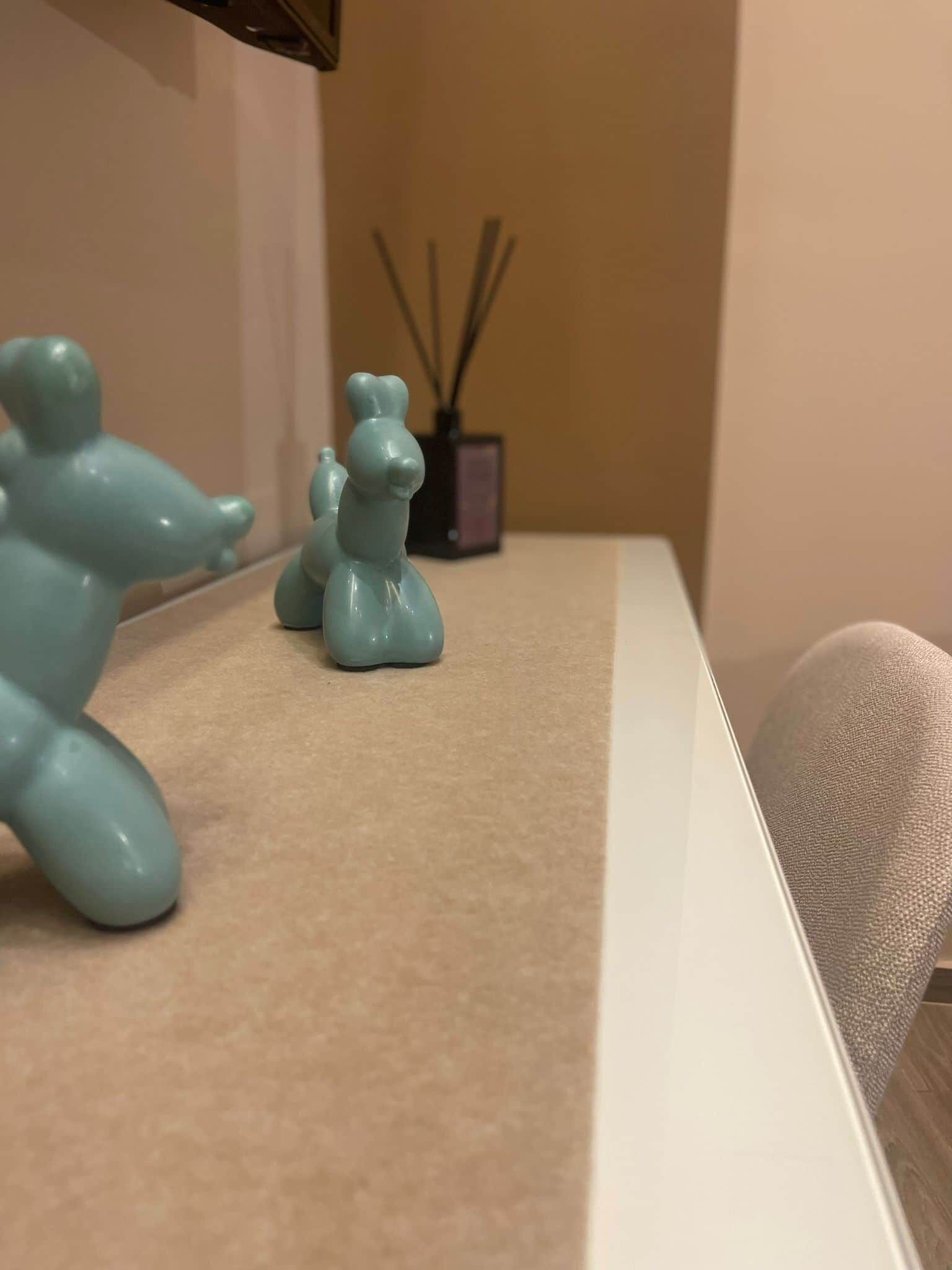 Una habitación con alfombra color beige, pared blanca y una pequeña mesa con objetos decorativos.