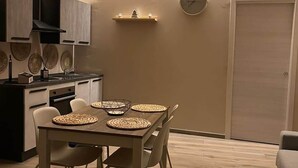 Una cucina compatta con elettrodomestici moderni, una zona pranzo con tavolo e sedie in legno, e un orologio appeso al muro.
