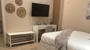 Una camera da letto con un letto, una scrivania, una sedia, una panca e una televisione appesa al muro.