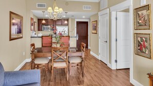 A spacious dining area with a wooden table and chairs, a chandelier, and a kitchen in the background. - Stylish 1BR condo in The Grand at Sandestin Golf & Beach Resort! (Miramar Beach)