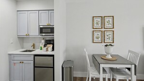 Une cuisine moderne avec des meubles blancs, un réfrigérateur en acier inoxydable et un four à micro-ondes. On y trouve une table à manger avec des chaises blanches et un vase posé dessus.