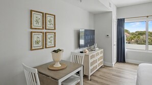 Une pièce moderne comprenant une table à manger, des chaises blanches, un téléviseur et, au mur, des reproductions encadrées de motifs botaniques.