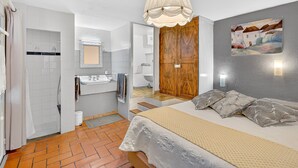 Ein Schlafzimmer mit Bett, einem Holzschrank, einem Badezimmer mit Waschbecken und Spiegel sowie einem Flur mit einer Tür.