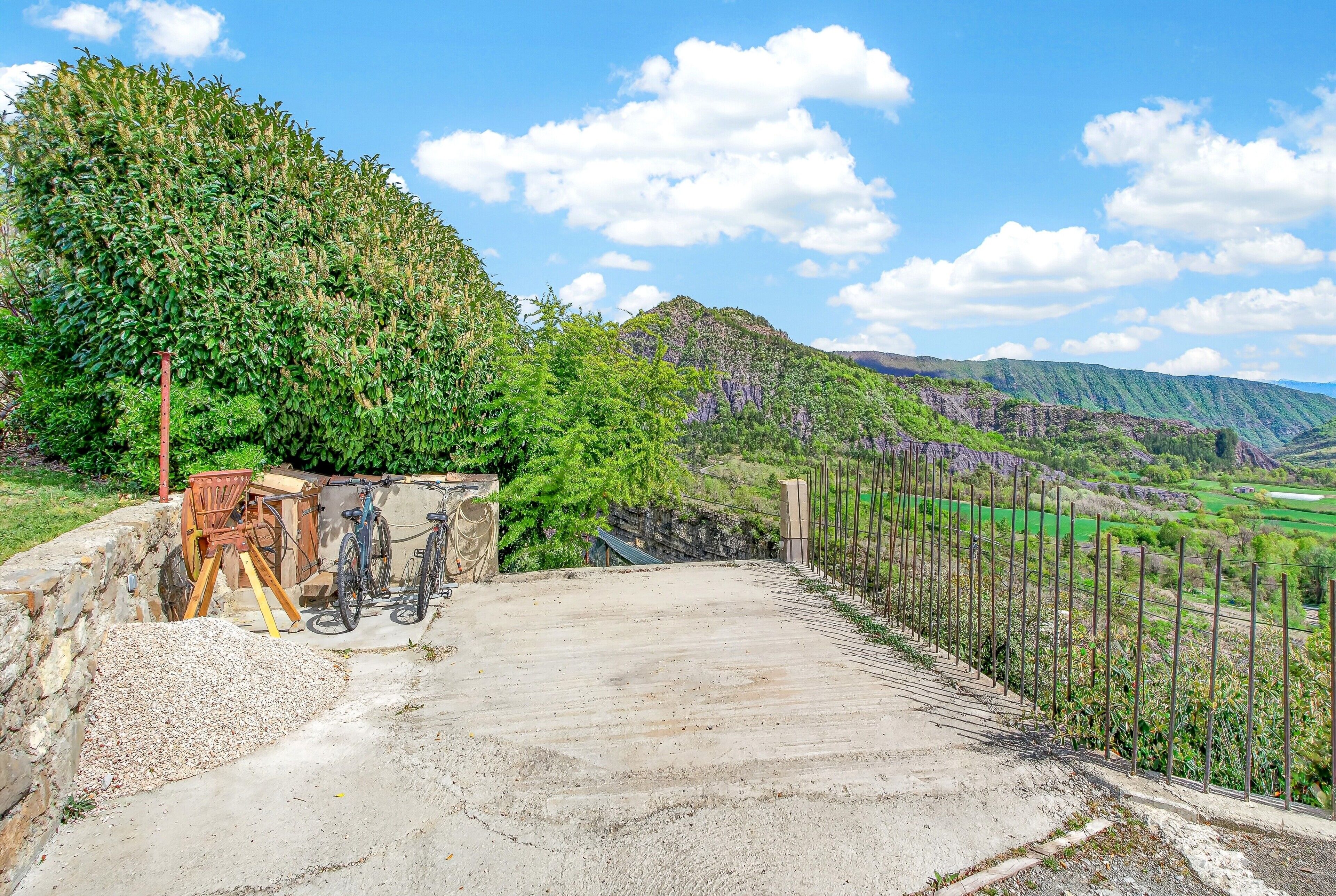 A concrete platform with a wooden chair and a bicycle, overlooking a green valley and hills.