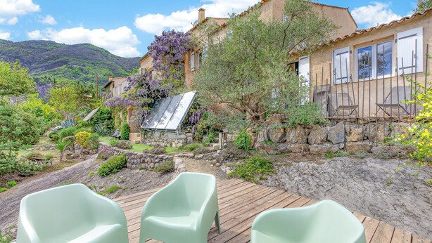 Ein rustikales Haus mit einer Holzdiele, einer Steinmauer und einem Garten mit verschiedenen Pflanzen und einer Pergola.