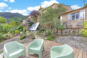 Ein rustikales Haus mit einer Holzdiele, einer Steinmauer und einem Garten mit verschiedenen Pflanzen und einer Pergola.