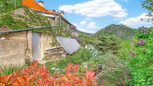 Ein Gebäude an einem Hang mit einem geneigten Dach, einer Solaranlage und einem Garten mit verschiedenen Pflanzen.