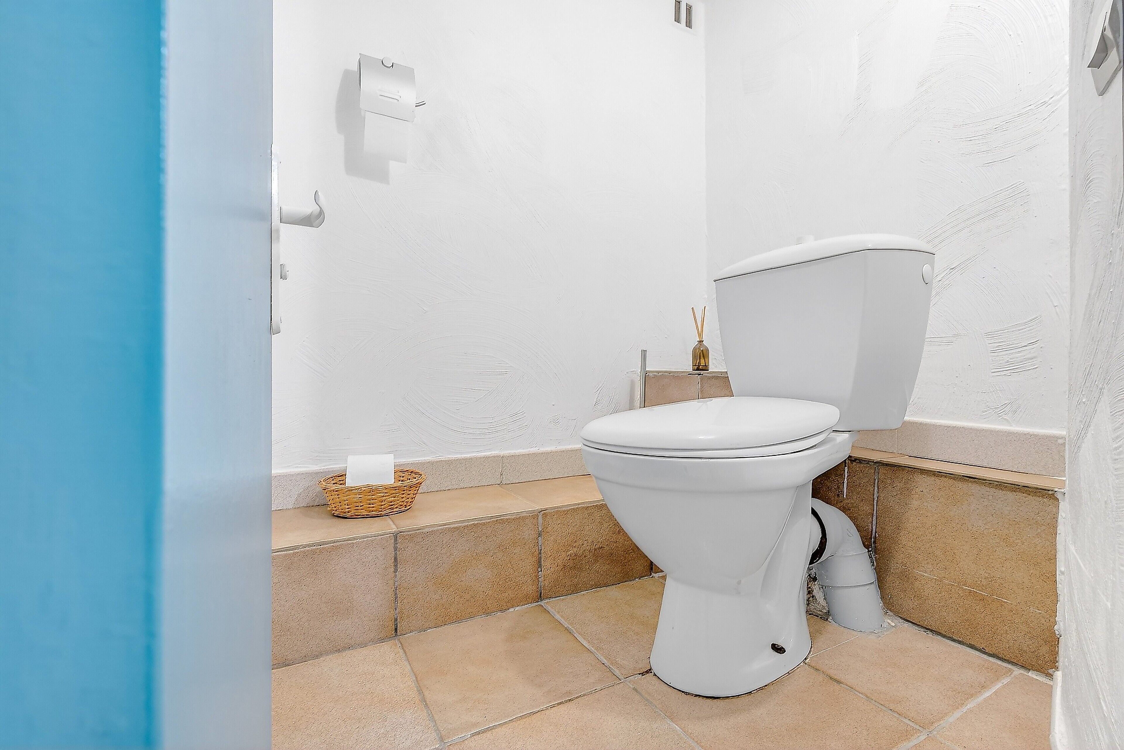 Un baño con un inodoro blanco, una cesta en el suelo y un dispensador de toallas en la pared.