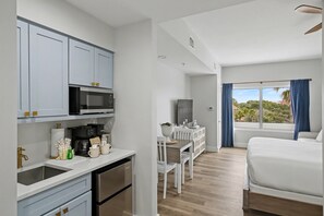 Eine moderne Küche mit weißen Schränken, einer Mikrowelle und einer Kaffeemaschine. Es gibt eine Essecke mit Tisch und Stühlen, und ein Bett mit weißer Bettwäsche.