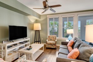 A living room with a flat-screen TV, a ceiling fan, a sofa, a patterned armchair, and a window with a view of trees. - 1BR Bahia Condo at Sandestin Golf & Beach Resort (Miramar Beach)