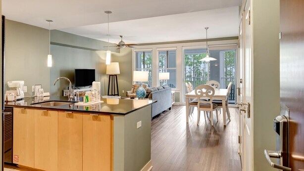 A modern kitchen with a central island, a dining area with a table and chairs, and a living room with a sofa and TV. - 2BR Bahia Suite at Golf & Beach Resort (Miramar Beach)