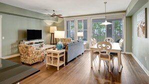 A living room with a sofa, TV, and dining area with chairs and a table. - 2BR Bahia Suite at Golf & Beach Resort (Miramar Beach)