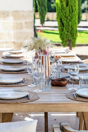 An outdoor dining table set with plates, glasses, and cutlery, surrounded by a stone wall and greenery. - Domaine Mas Lafleur - Mas Provençal for 12 people - Swimming pool & large garden (Châteaurenard)