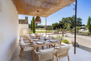 Un espace de restauration en plein air avec une table dressée pour six personnes, entourée de chaises en osier, sous un auvent en fibres tressées.