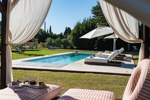 Et poolområde med liggestole, et bord med et glas vin og udsigt til en swimmingpool.