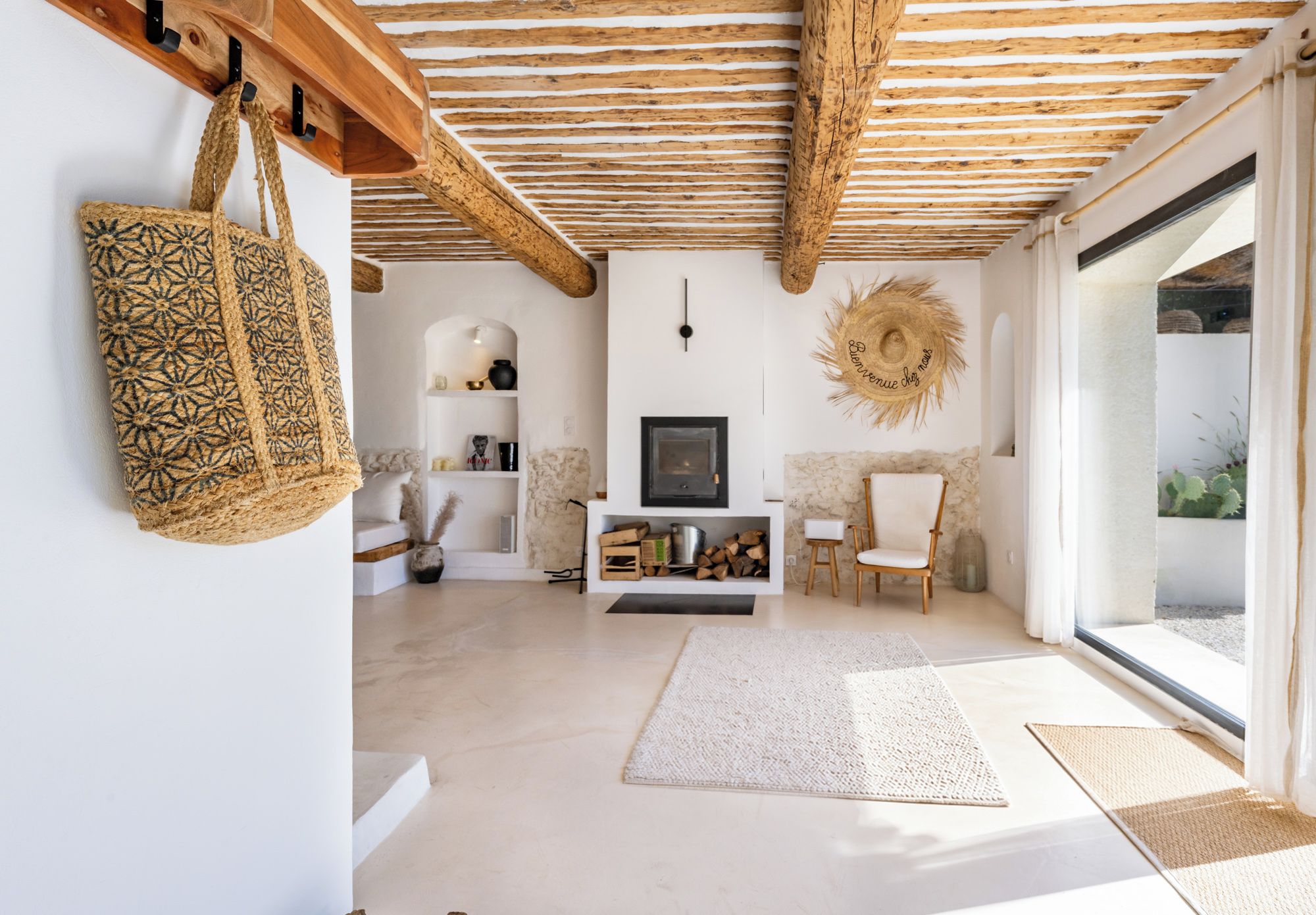 Un vaste salon doté d’un plafond en bois, d’une cheminée, d’un grand panier en osier et offrant une vue à travers une porte vitrée.