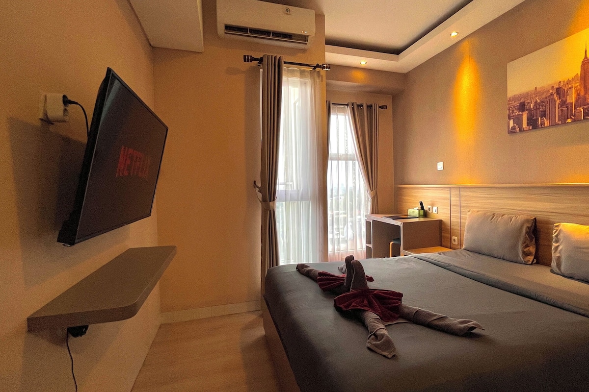 A hotel room with a bed, a desk, a TV, and a cityscape painting.