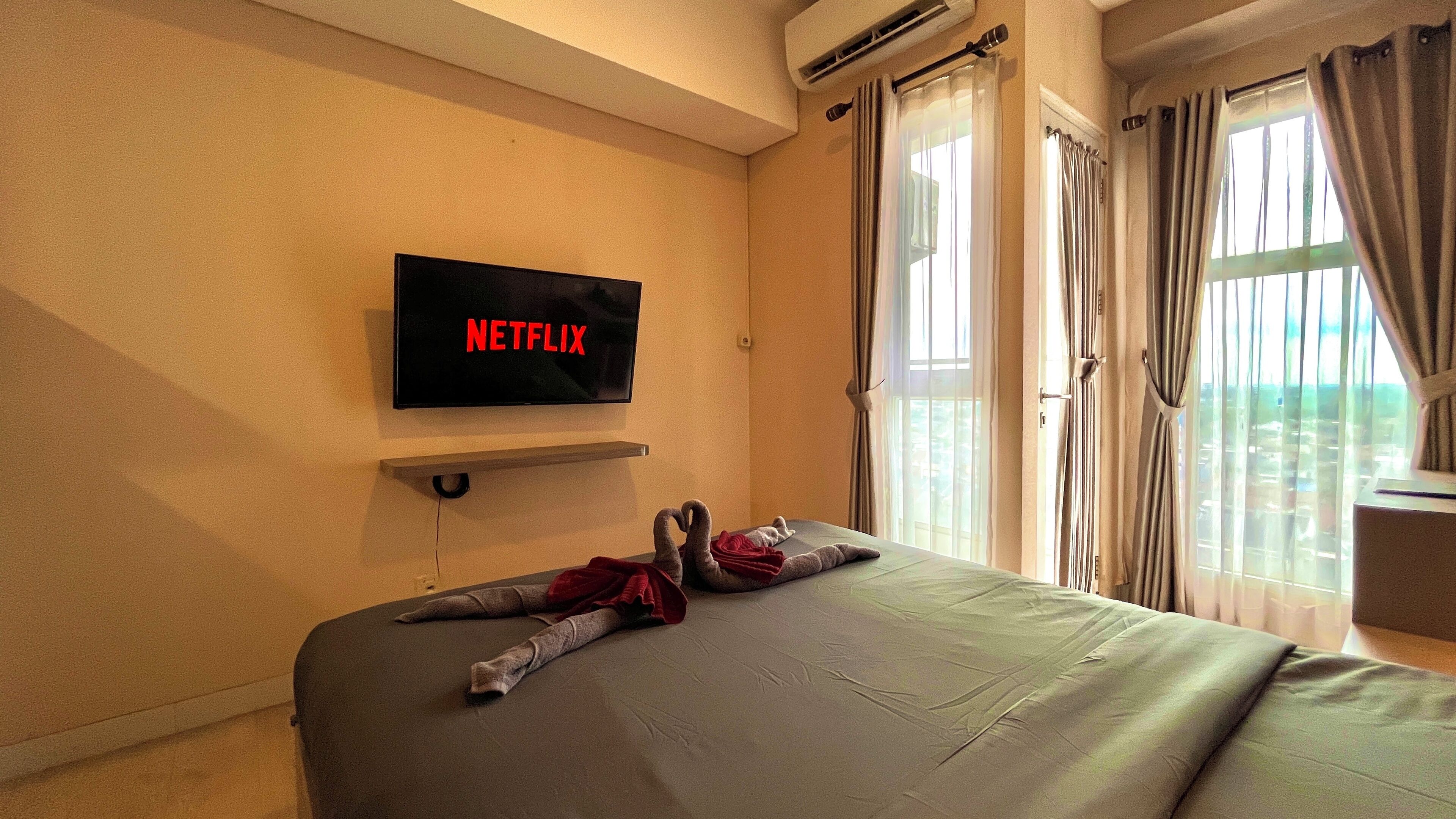 A hotel room with a bed, a mounted TV displaying 'NETFLIX', and a window with curtains.