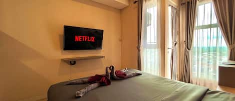 A hotel room with a bed, a mounted TV displaying 'NETFLIX', and a window with curtains.