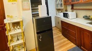 A compact kitchen with a refrigerator, microwave, and oven. There is a wooden cabinet with glass doors and a small shelf with decorative items. - Cozy Pagadian City Apartment for Rent - Perfect for Families (Pagadian)