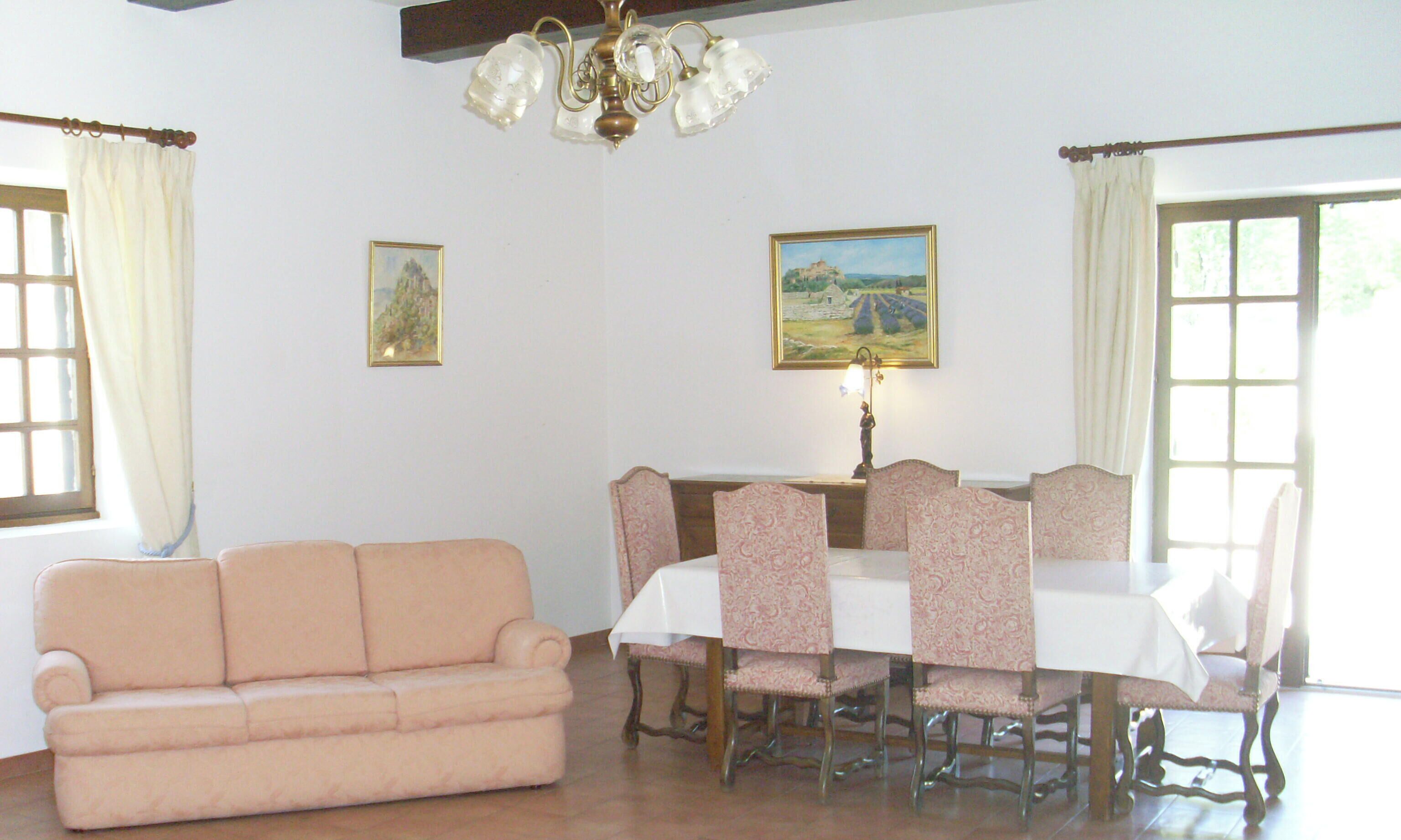 A dining area with a table set for six, surrounded by patterned chairs, a sofa, and two paintings on the walls.