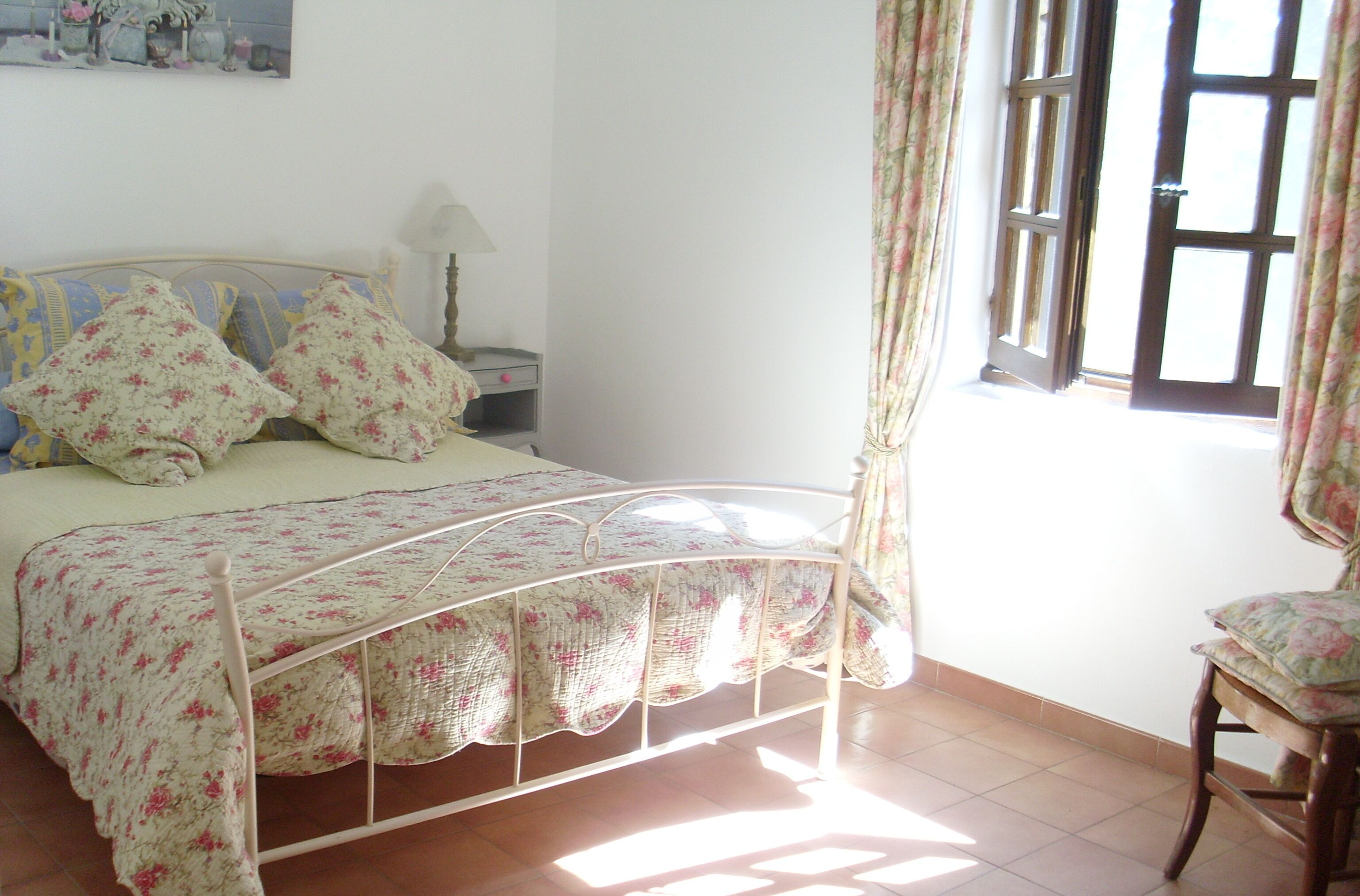 Une chambre à coucher avec un lit, une chaise, une table de chevet et une fenêtre avec des rideaux.