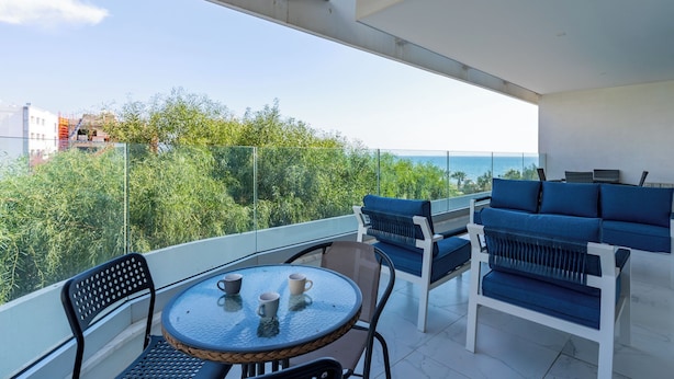 A balcony with a glass table, chairs, and a sofa, overlooking a cityscape and greenery. - Starlet 1-BR Apt. & Pool in Larnaca (Larnaca)
