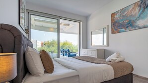 A bedroom with a bed, a nightstand, a lamp, a large window, and a painting on the wall. - Starlet 1-BR Apt. & Pool in Larnaca (Larnaca)