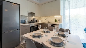 A modern kitchen with a refrigerator, microwave, stove, and sink. There is a dining table set with plates, glasses, and cutlery. - Starlet 1-BR Apt. & Pool in Larnaca (Larnaca)